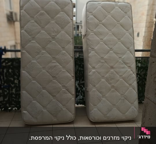 שני מזרנים עומדים על מרפסת לרקע בניינים